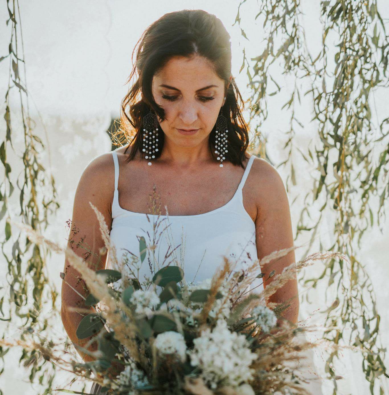 Frau mit Brautstrauss im weissen Kleid unter haengenden Zweigen